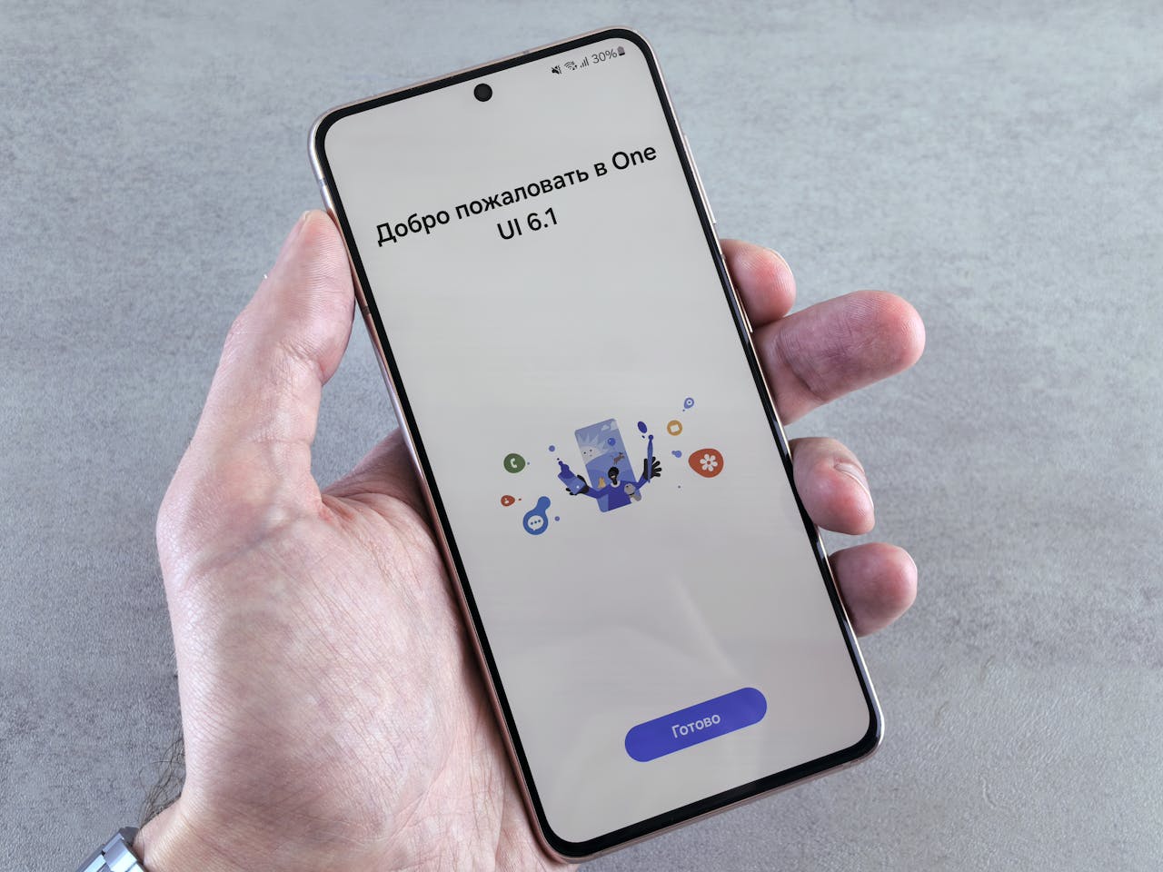 A close-up of a hand holding a smartphone displaying One UI 6.1 setup screen with Cyrillic text.